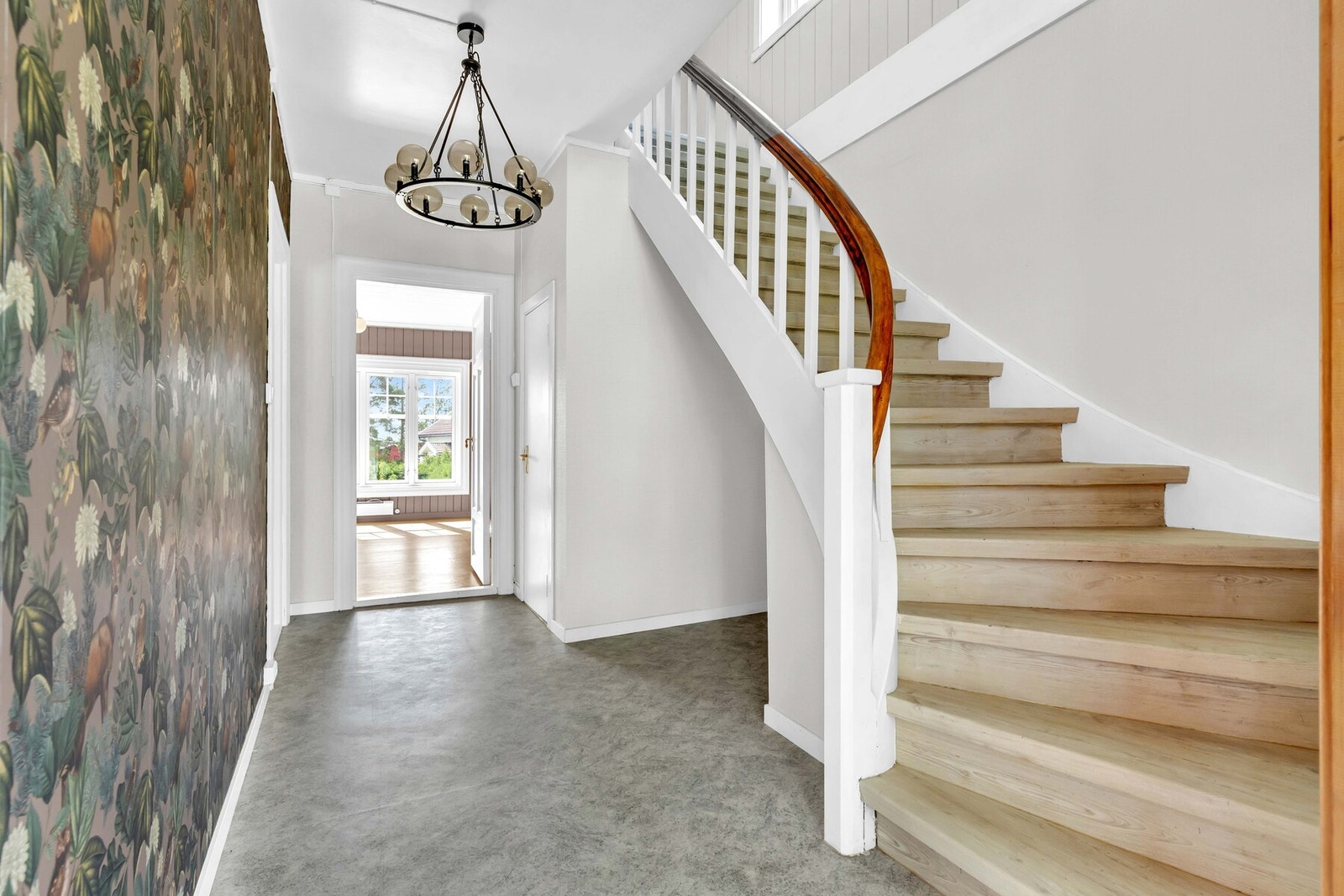 Hovedentréen har et tiltalende uttrykk med blomstrete tapet på veggene og gulvbelegg i matchende farger. Den stilige trappen opp til loftetasjen ble fornyet i ca 2019. Galleribilde
