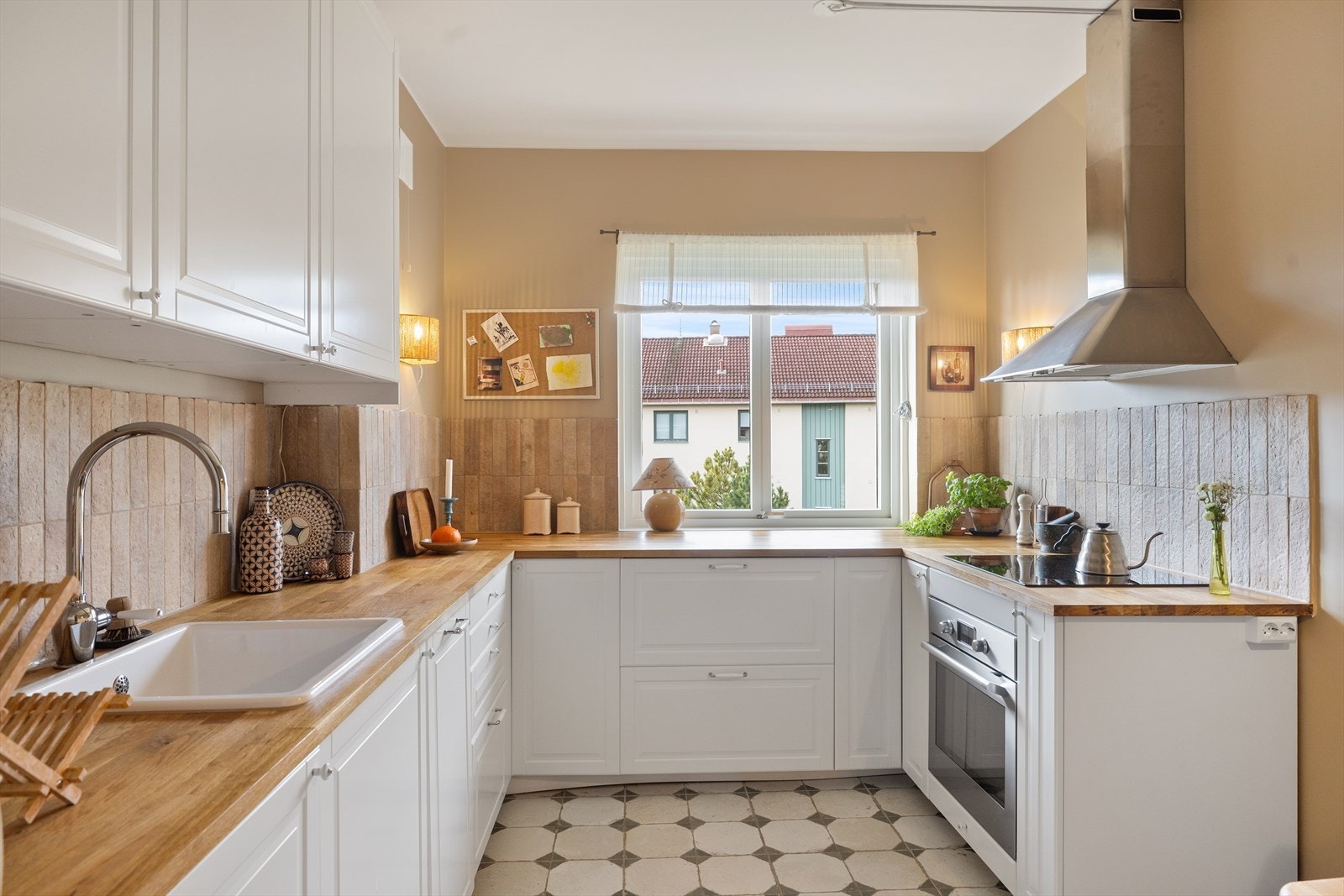 Tidsriktig innredning med hvite, profilerte fronter, fliser på vegg over kjøkkenbenken og benkeplate i tre. Galleribilde