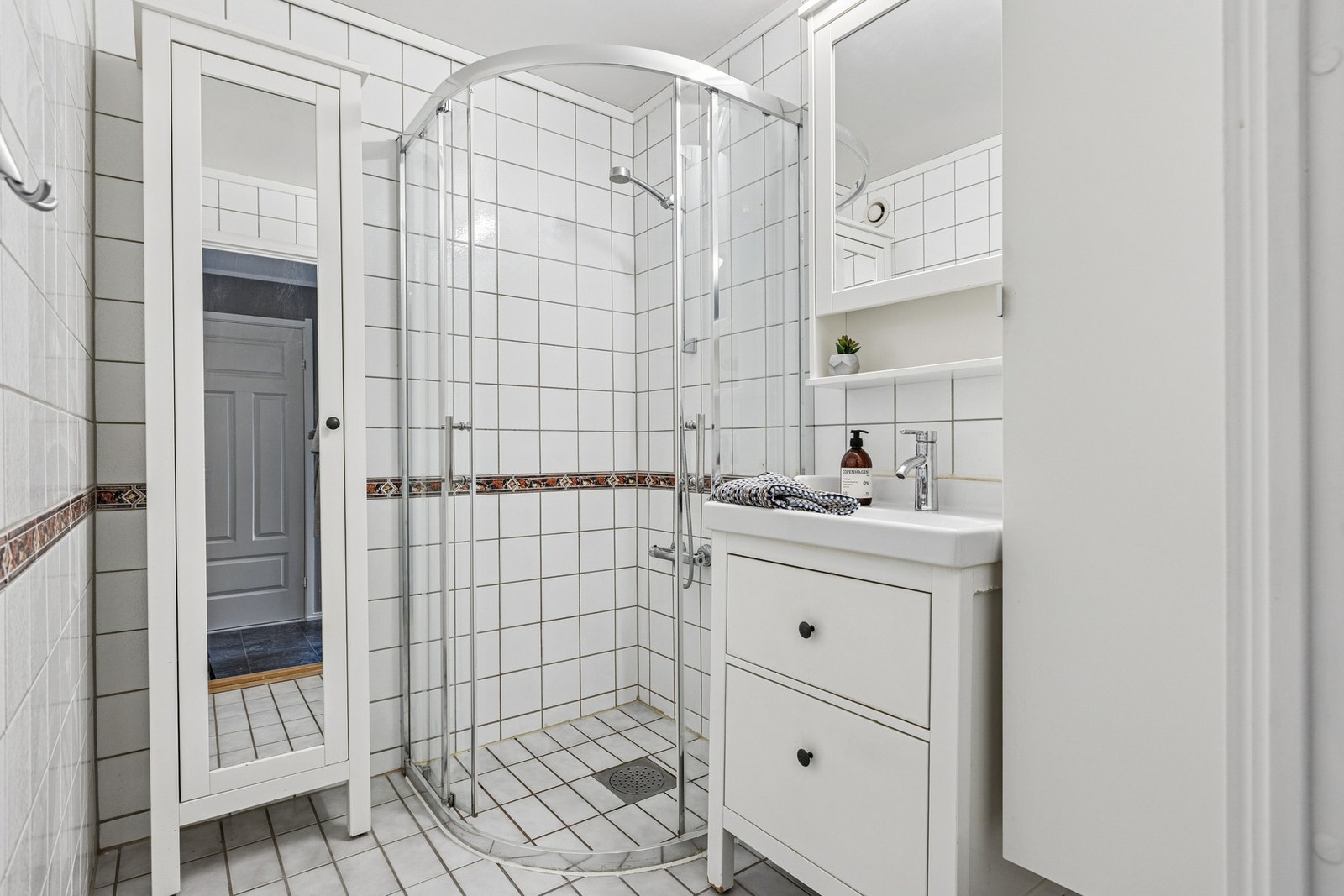 Lyst baderom utstyrt med dusjhjørne og servant i servantskap. Galleribilde