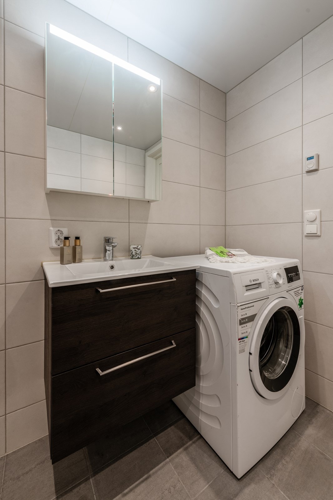 Servantinnredning, vegghengt toalett og dusj med glassdør, samt opplegg for vaskemaskin og tørketrommel Galleribilde