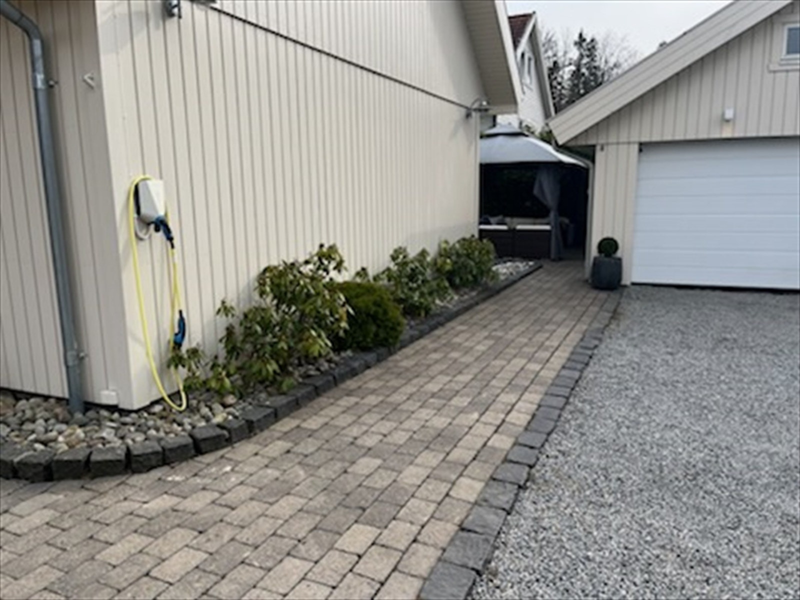 Pent opparbeidet uteareal, med Herregaardsten, gruset innkjørsel, bedd og beplantinger. Galleribilde