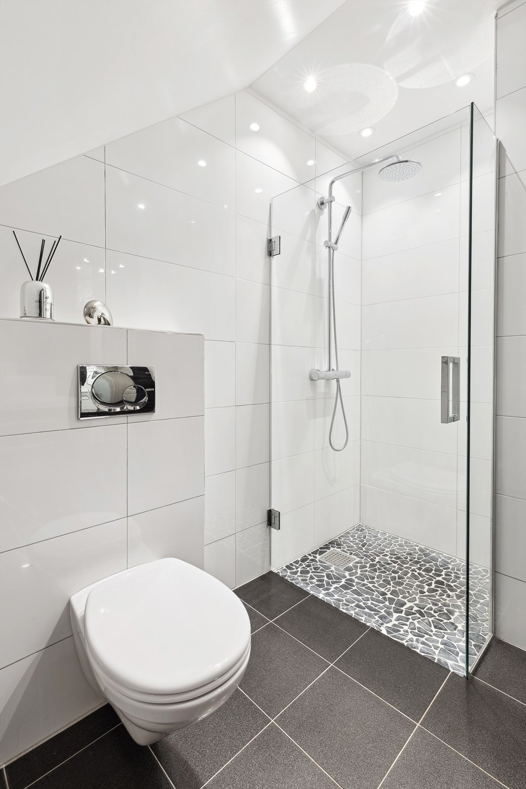 Lekkert, flislagt bad med dusjhjørne med regndusj, moderne servantinnredning med ovenpåliggende servant samt vegghengt toalett. Galleribilde