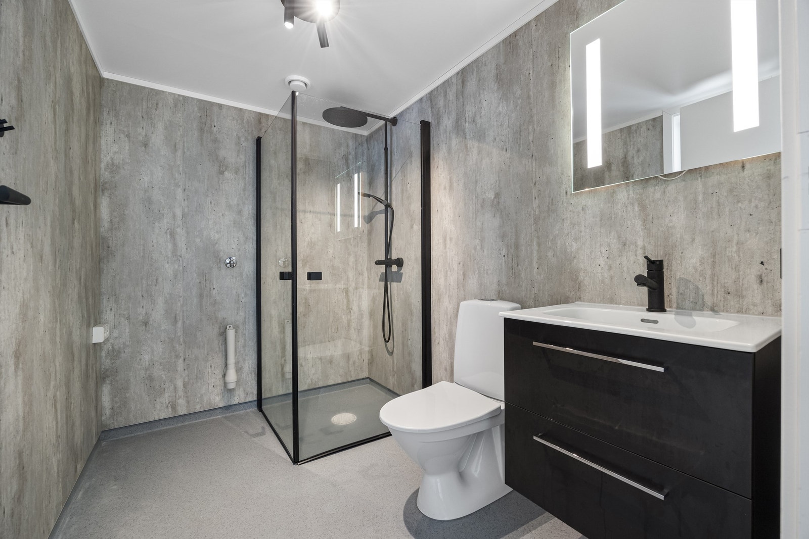 Baderom utstyrt med servantinnredning, toalett, dusjhjørne, speil med lys og opplegg for vaskemaskin Galleribilde