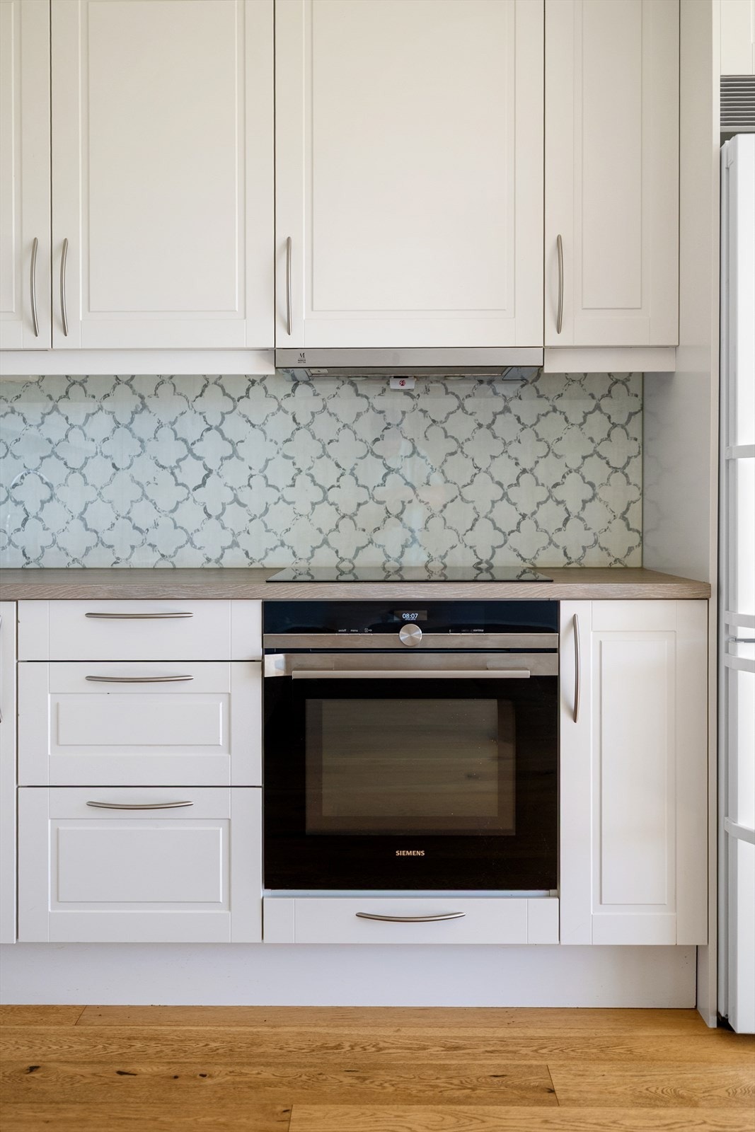 De profilerte frontene gir kjøkkenet et klassisk og elegant uttrykk, mens benkeplaten i laminat med nedlimt oppvaskkum og glassplate mellom benk og overskap gir en praktisk og moderne finish. Galleribilde