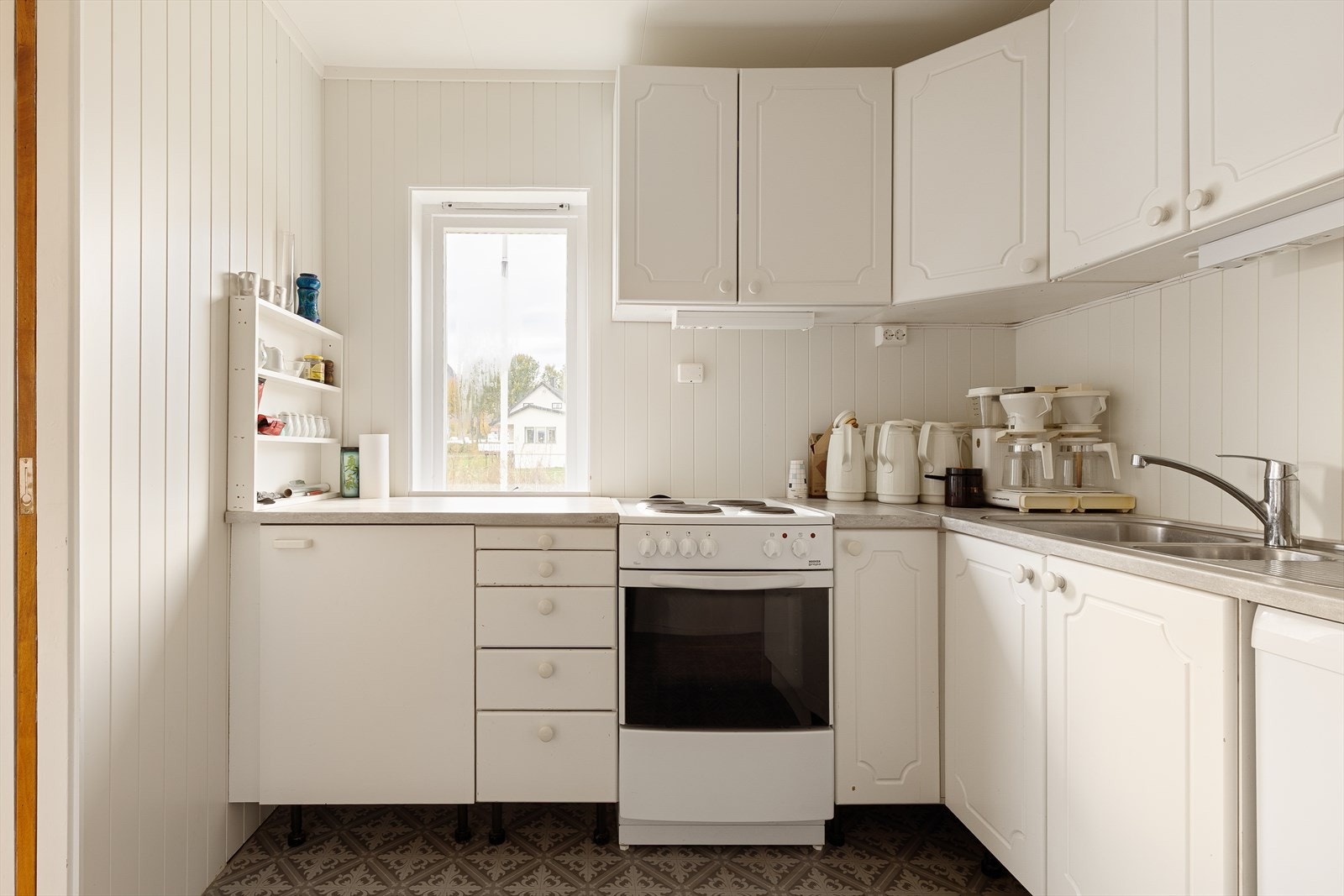 Kjøkken med kjøkkeninnredning i type hvit profil utførelse, normalt utbygget med benker og overskap. Plass for oppvaskmaskin. Galleribilde