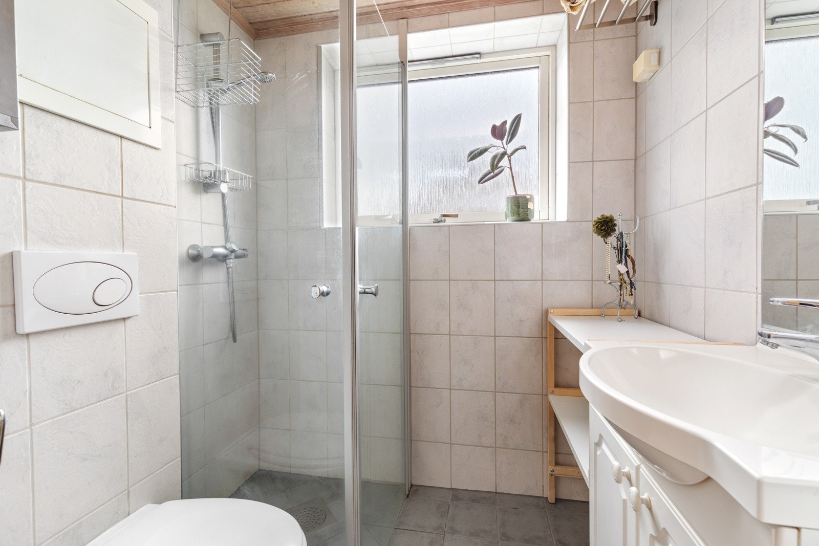 Flislagt bad med varme i gulv. Badet er innredet med servant over servantskap, vegghengt toalett, dushjørnet og opplegg til vaskemaskin. Galleribilde