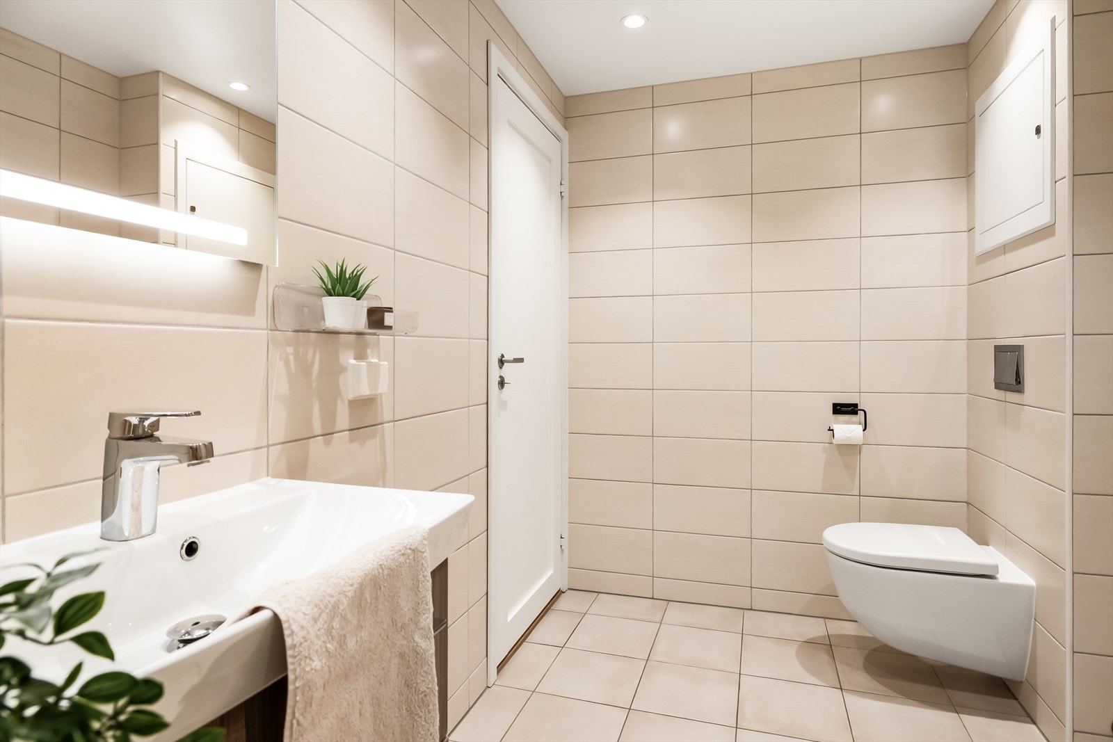 Badet inneholder veggmontert toalett, dusjhjørne, nedfelt servant med skap, og opplegg for vaskemaskin. Galleribilde