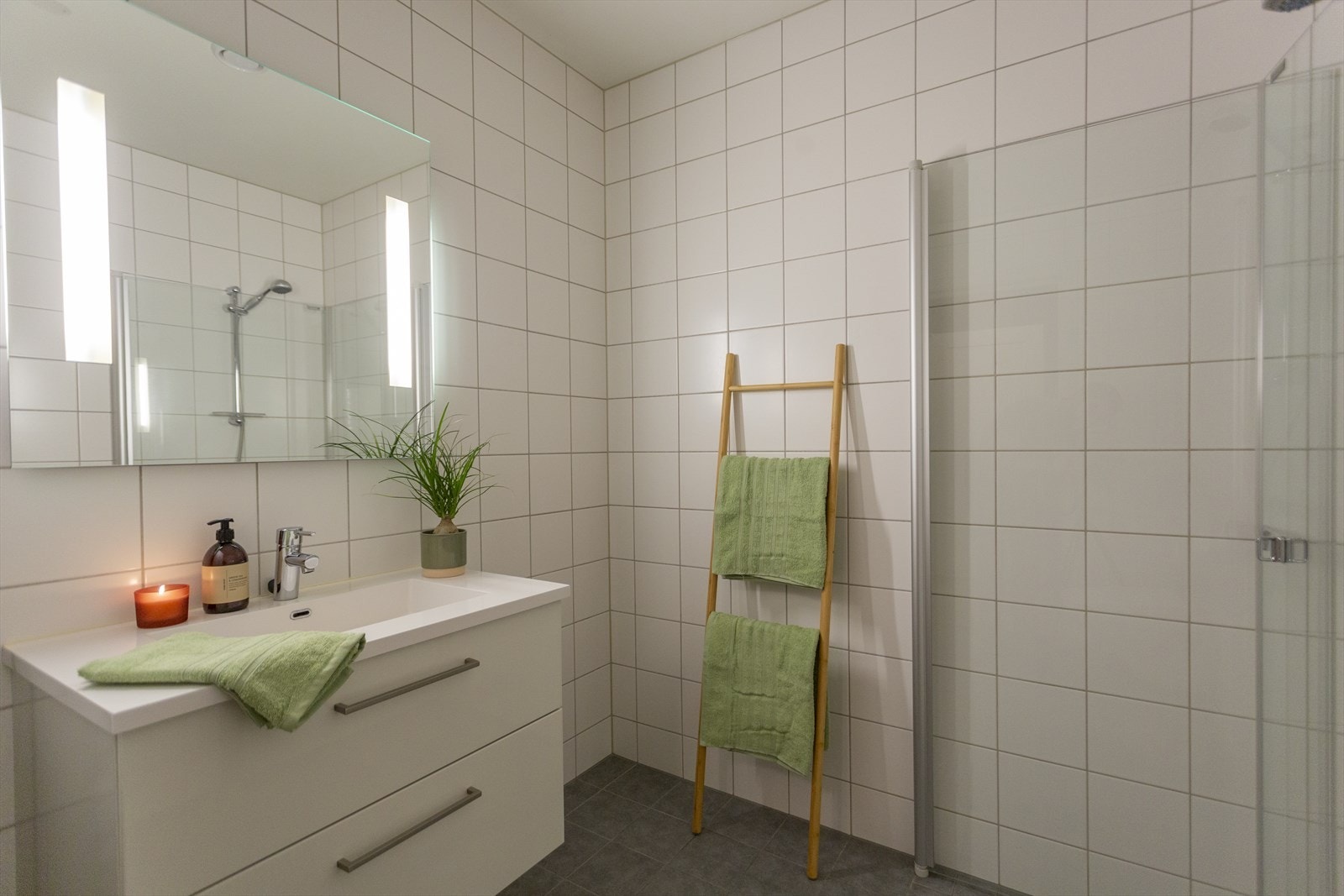 Badet er utstyrt med baderomsinnredning med skuffer og heldekkende servant. I overkant av servanten er det speil med lys. Dusjhjørne med innfellbare dusjdører med veggmontert dusjbatteri. Galleribilde