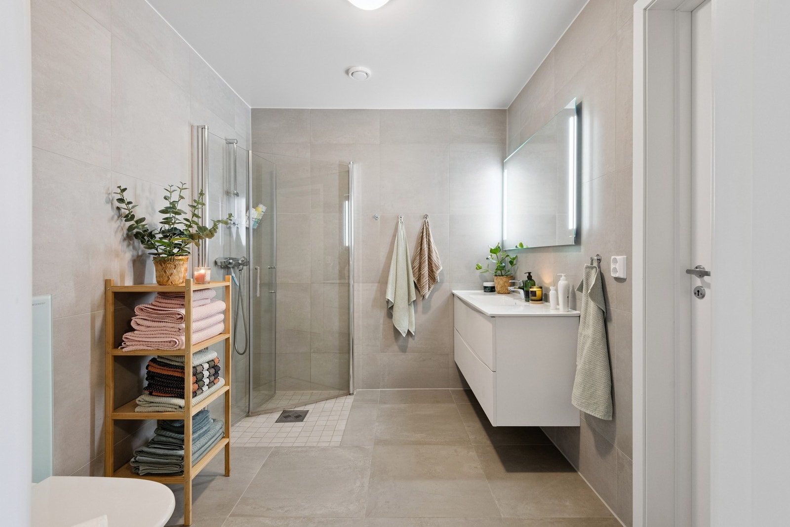 Romslig bad med flis på gulv og varmekabler. Badet har vegghengt toalett og dusjhjørne. Galleribilde