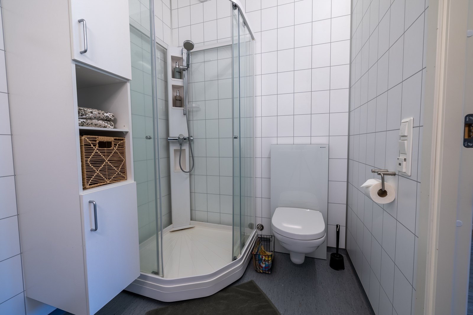 Badet har vegghengt toalett, dusjkabinett og baderomsskap på vegg. Galleribilde