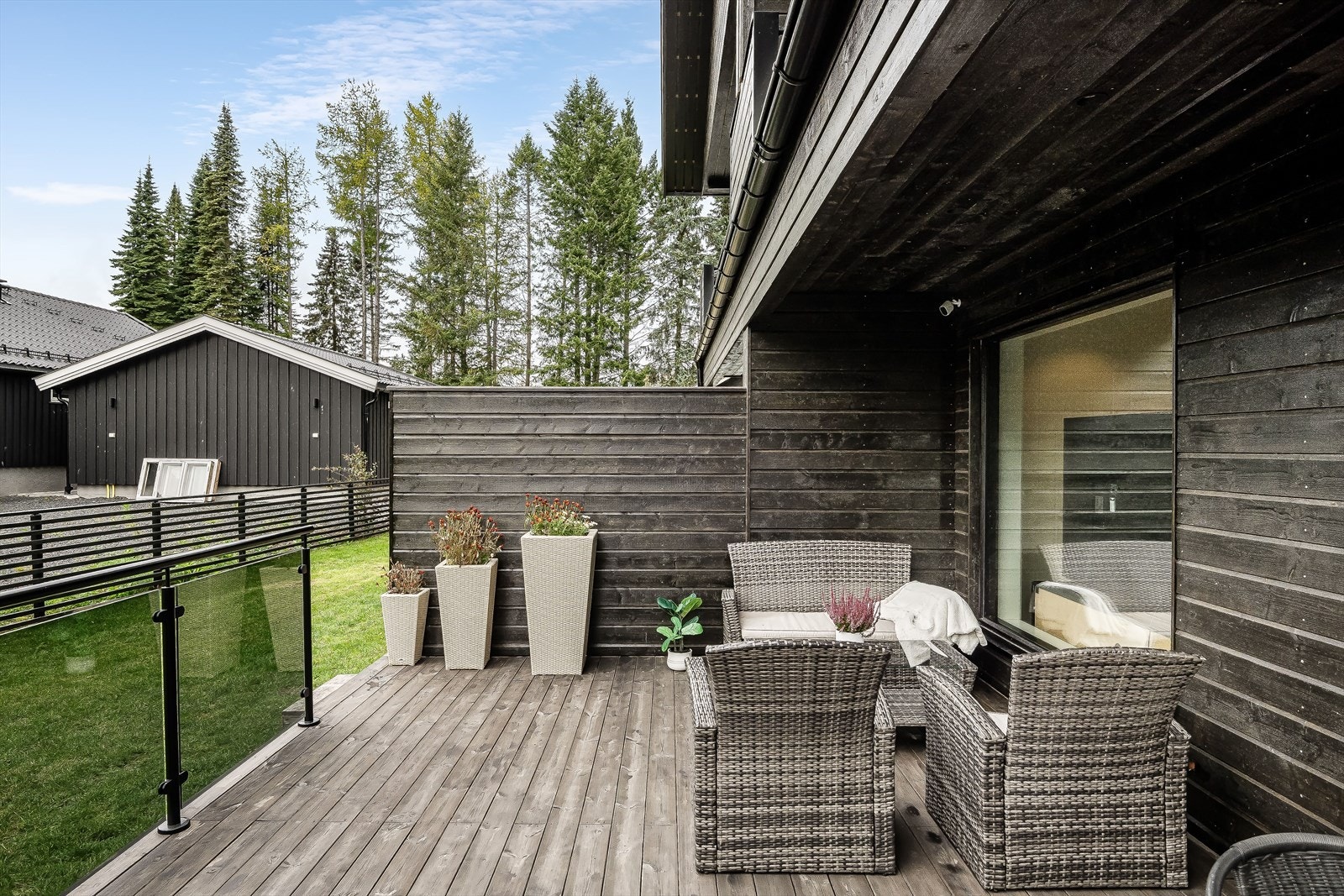 Terrassen er delvis overbygget, har terrassebord på gulv og stilig rekkverk med glassfelt. Det er også montert utebelysning og utvendig stikkontakt. Galleribilde