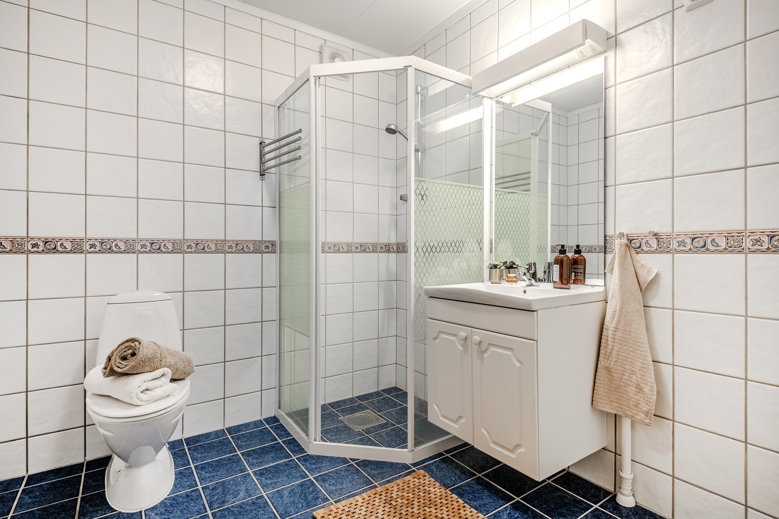 Badet har flislagte overflater, varmekabler og innredning med benkeskap, speil og belysning, dusj, servant, gulvstående toalett og opplegg for vaskemaskin. Galleribilde