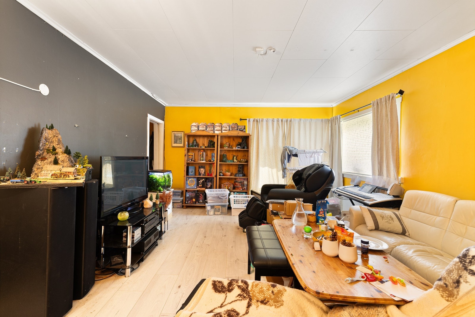 Romslig stue med karakterfullt gult veggparti, lyst gulv og takess i himlingen. Galleribilde