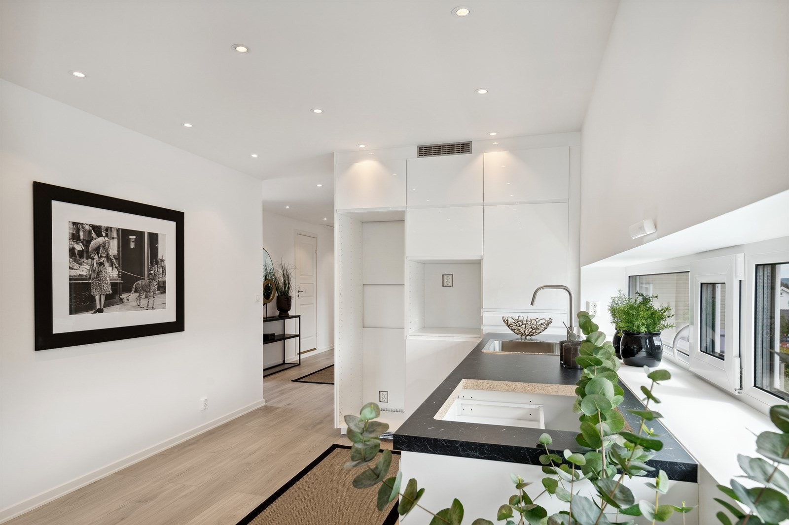 Kjøkkeninnredningen inneholder hvit laminat skapinnredning, laminat benkeplate, nedfelt kum og fliser over benk. Galleribilde