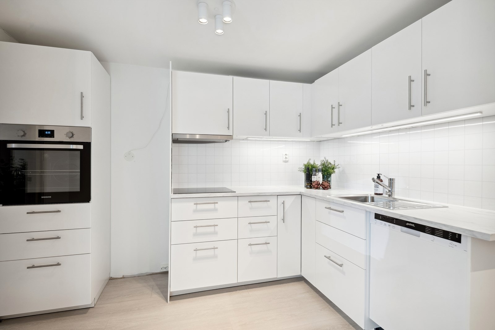 Ikeakjøkken fra 2020. Innredningen er i en tidløs stil med hvite, glatte fronter, laminatbenkeplater og nedfelt oppvaskkum. Galleribilde