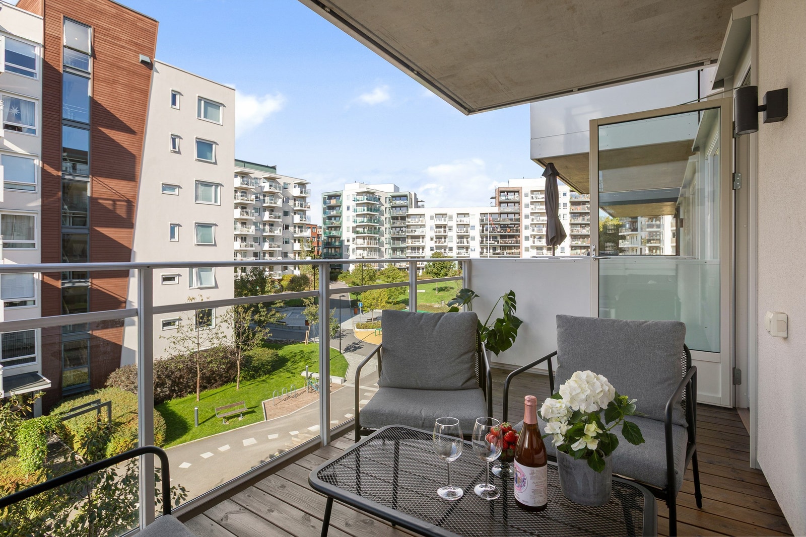 Vestvendt uteplass med utsikt over gårdstun. Gulv med terrassebord. Rekkverk i stål med innfelte glassplater. Belysning og stikkontakter. Galleribilde