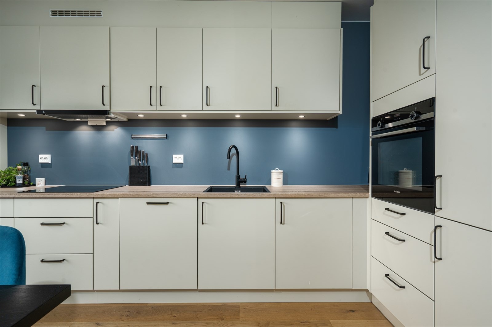 Pen og funksjonell kjøkkeninnredning med glatte fronter og benkeplate i laminert spon. Kjøkkenet er utstyrt med integrerte hvitevarer i form av oppvaskmaskin, kjøl/frys, koketopp og stekeovn. Galleribilde