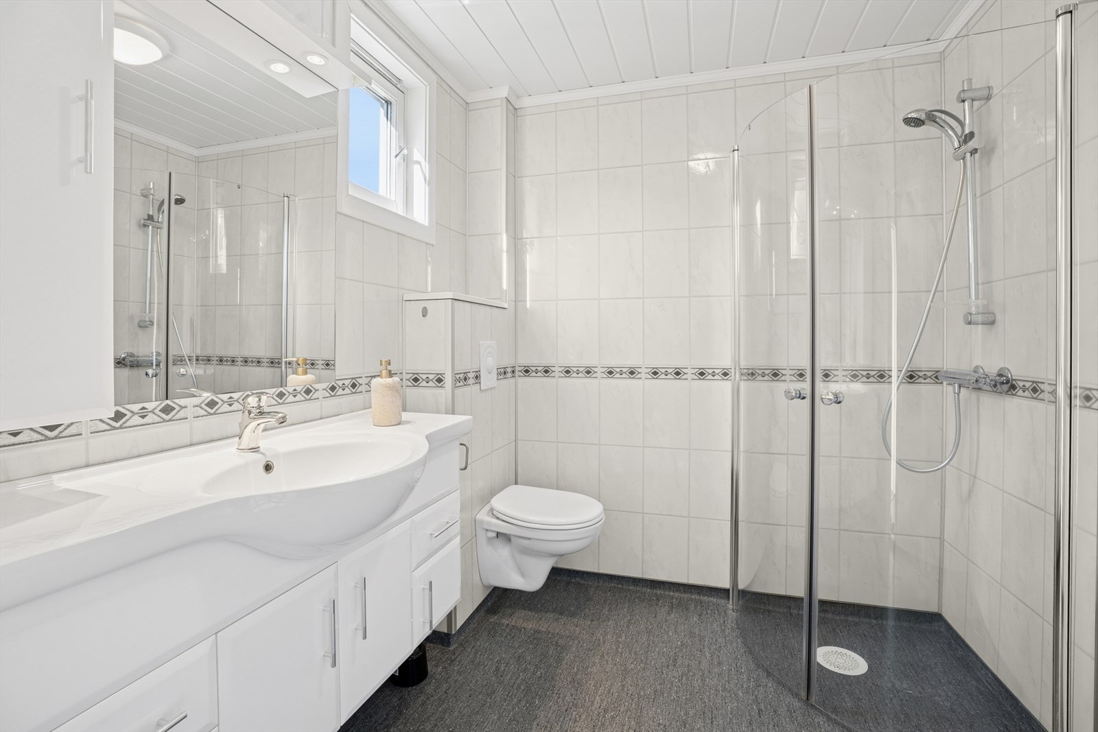 Bad med baderomsplater på veggene og vinylbelegg på gulv med gulvvarme. Galleribilde