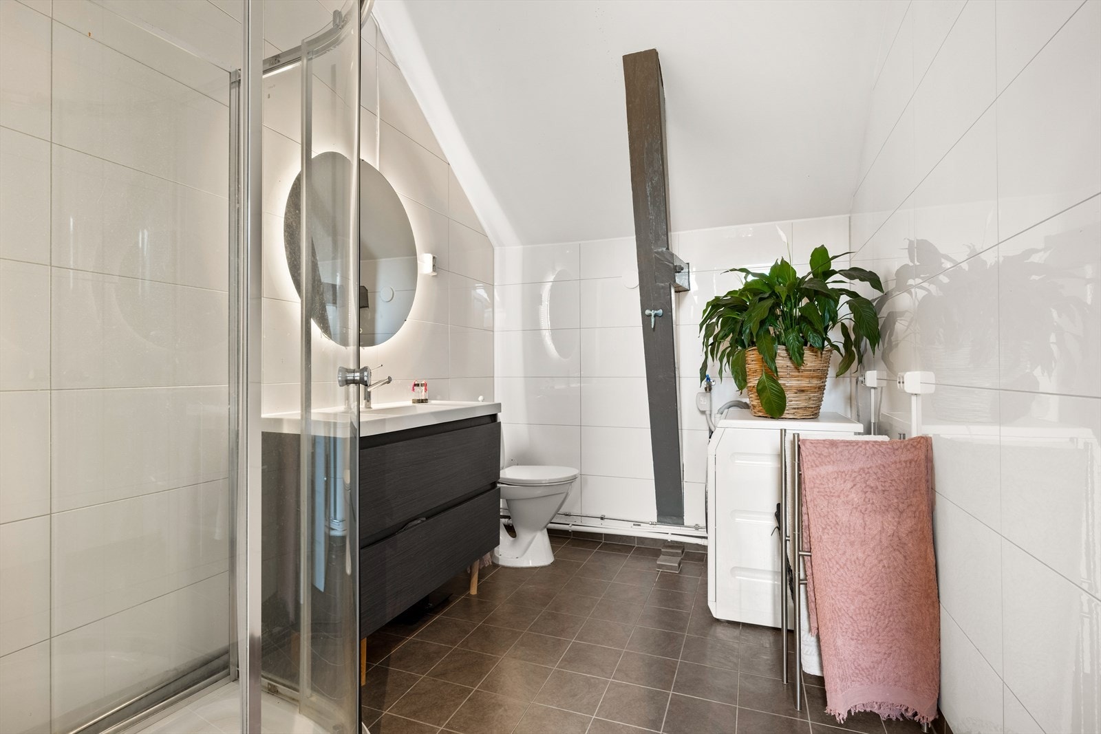 Flislagt bad med gulvvarme, dusjkabinett, WC, opplegg for vaskemaskin og moderne innredning med servantskap og speil med belysning. Galleribilde