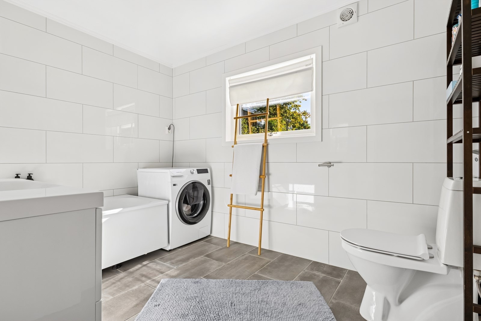 Det er også opplegg for vaskemaskin, noe som gjør badet godt tilrettelagt for daglig bruk. Ventilasjonen ivaretas av en elektrisk styrt avtrekksvifte, som sikrer god luftkvalitet og fuktregulering. Galleribilde