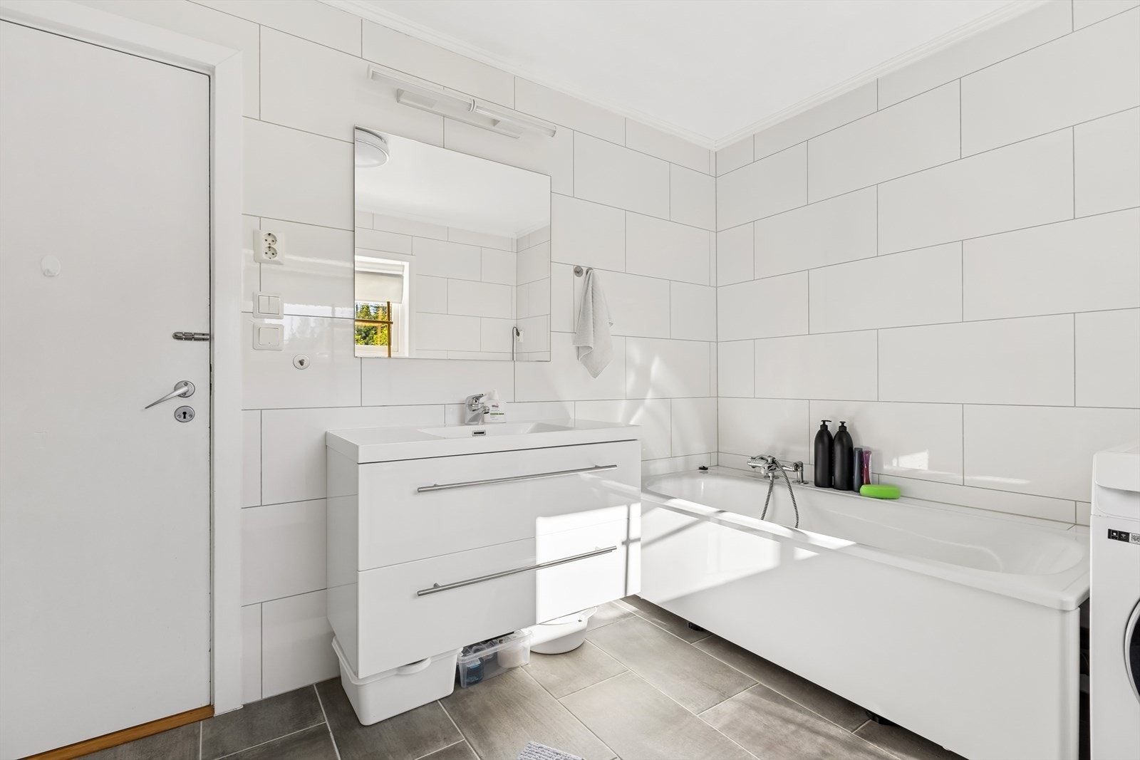Badet i hovedetasjen fremstår som romslig med flislagte gulv og slette, malte plater i himlingen som gir et rent og moderne uttrykk. Rommet er utstyrt med servantinnredning, gulvmontert toalett og badekar. Galleribilde