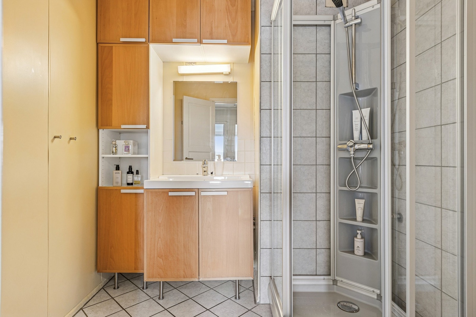 Rommet er praktisk innredet med vegghengt servantinnredning, ovenpåliggende servant, speil med belysning og stikkontakt, samt et vegghengt høyskap som gir god oppbevaringsplass. Dusjkabinett med dusjarmatur sørger for en funksjonell løsning. Galleribilde