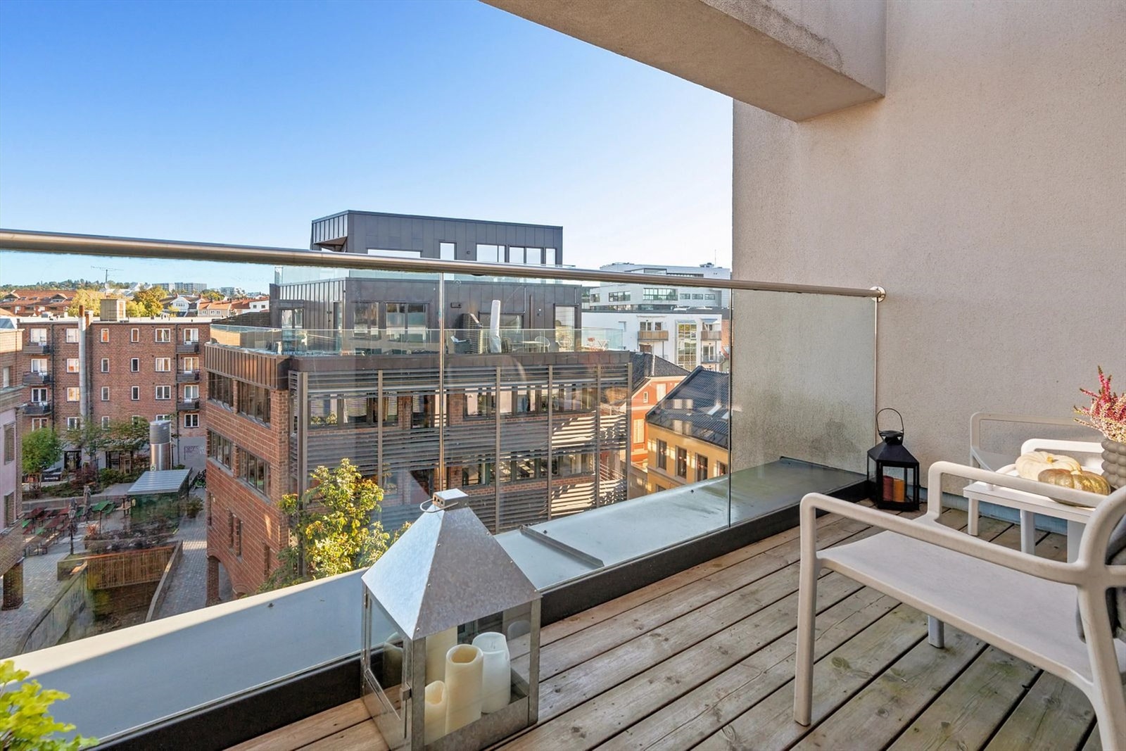 Balkong med glassrekkverk og tregulv, og romslig utsikt mot byen - perfekt for avslapping eller følge med på bylivet. Galleribilde