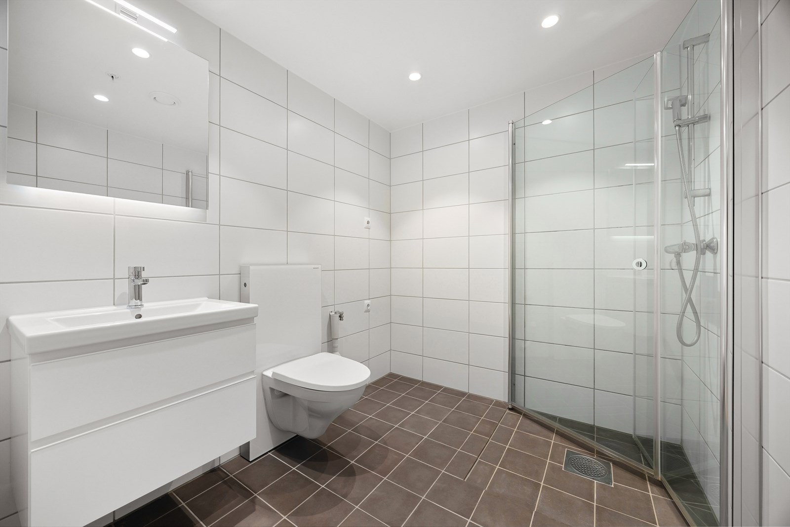 Lyst helfliset bad av god størrelse utstyrt med dusjhørne, servant med skuffer, opplegg for vaskemaskin og wc. Varme i gulv og downlights i tak. Galleribilde