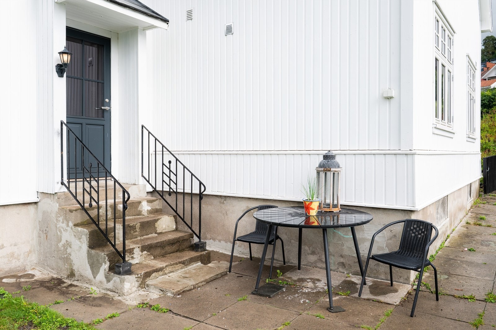 Gangvei langs med boligens vestside er lagt med steinheller, som tar deg frem til inngangspartiet som ligger på boligens vestside. Her er det støpt betongtrapp opp til inngangsdøren med rekkverk på sidene, og ny inngangsdør fra 2022. Galleribilde