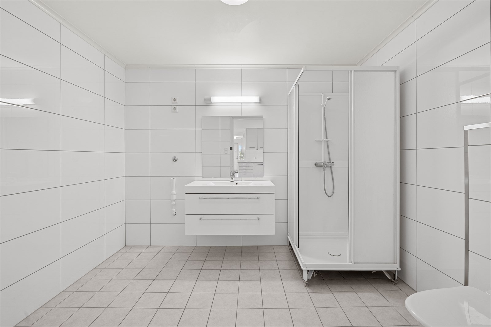 Utleiedel: Badet kombinerer funksjon og komfort, med fliser på både gulv og vegger som gir et helhetlig og lettstelt uttrykk. Rommet er innredet med vegghengt toalett, dusjkabinett og baderomsinnredning med nedfelt servant. Galleribilde