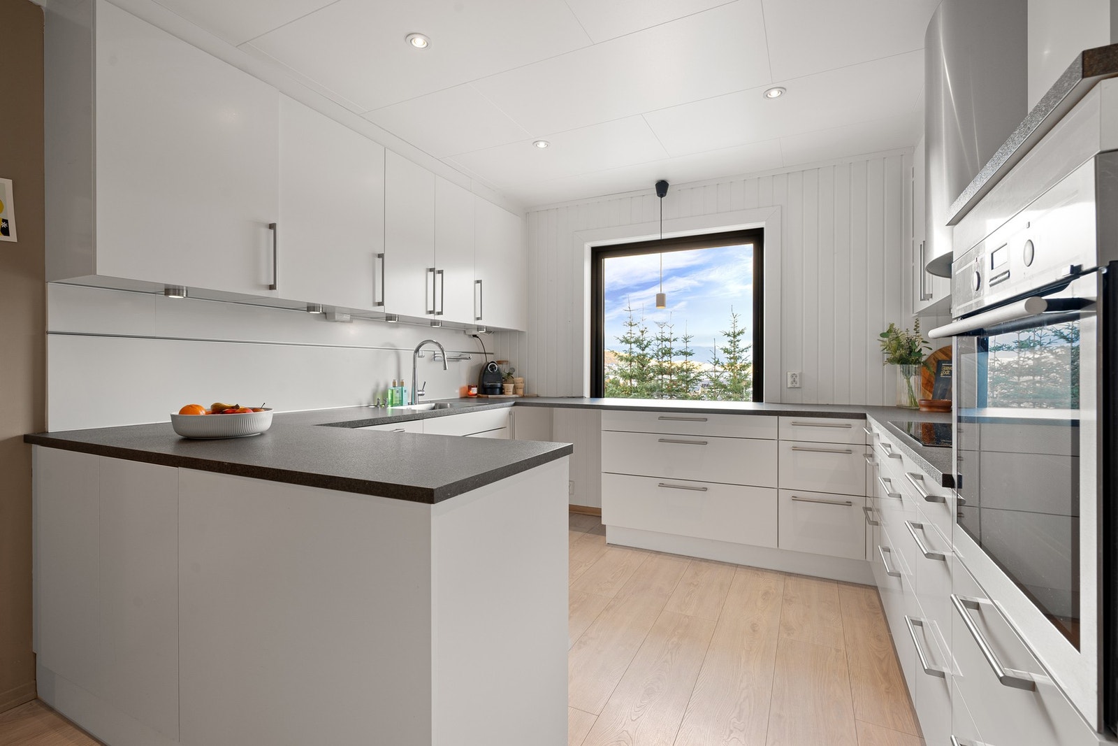 Flott kjøkken med halvøy og innredning med lyse, slette fronter, takhøye overskap og benkeplate av laminat Galleribilde