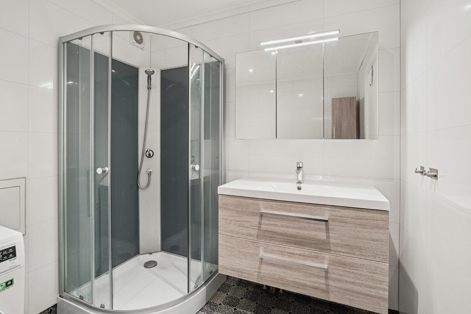 Baderom i 2. etasje har belegg på gulv, baderomsplater på vegger og malte plater med innfelte downlights i himling. Rommet er innredet med klosett, servant på innredning og dusjkabinett. Galleribilde