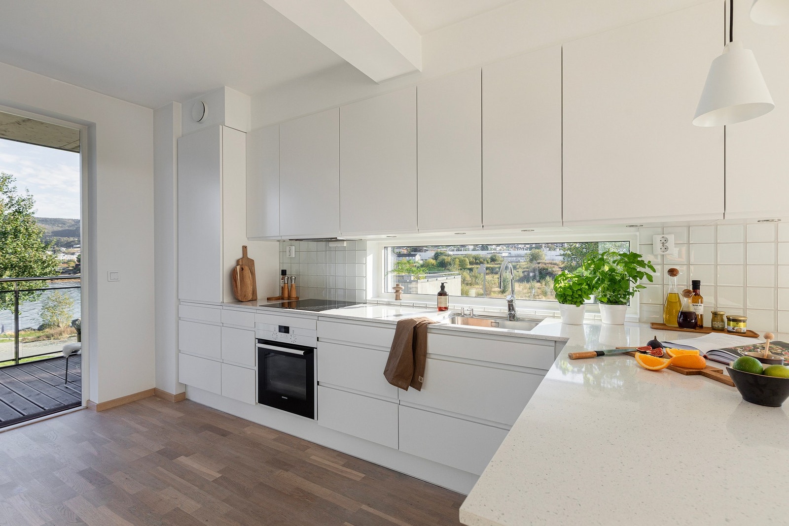 Kjøkkenet er utvidet med flere skap og kjøkkenøy, oppgradert innredning fra skap til skuffer, benkeplate i Silestone kompositt og hvit komfyr. Hvite glassfliser over benk. Galleribilde