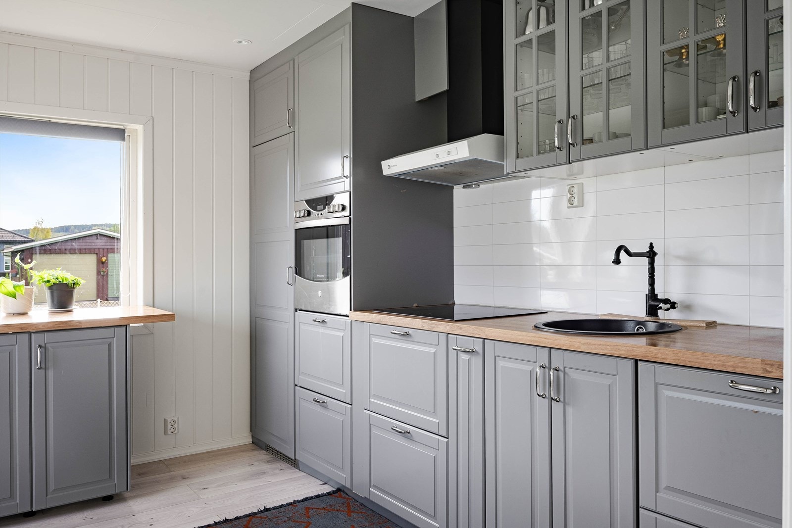 Pen kjøkkeninnredning med god skap- og benkeplass. Innredningen har grå profilerte fronter og benkeplate av laminert tre med nedfelt rund oppvaskkum. Galleribilde