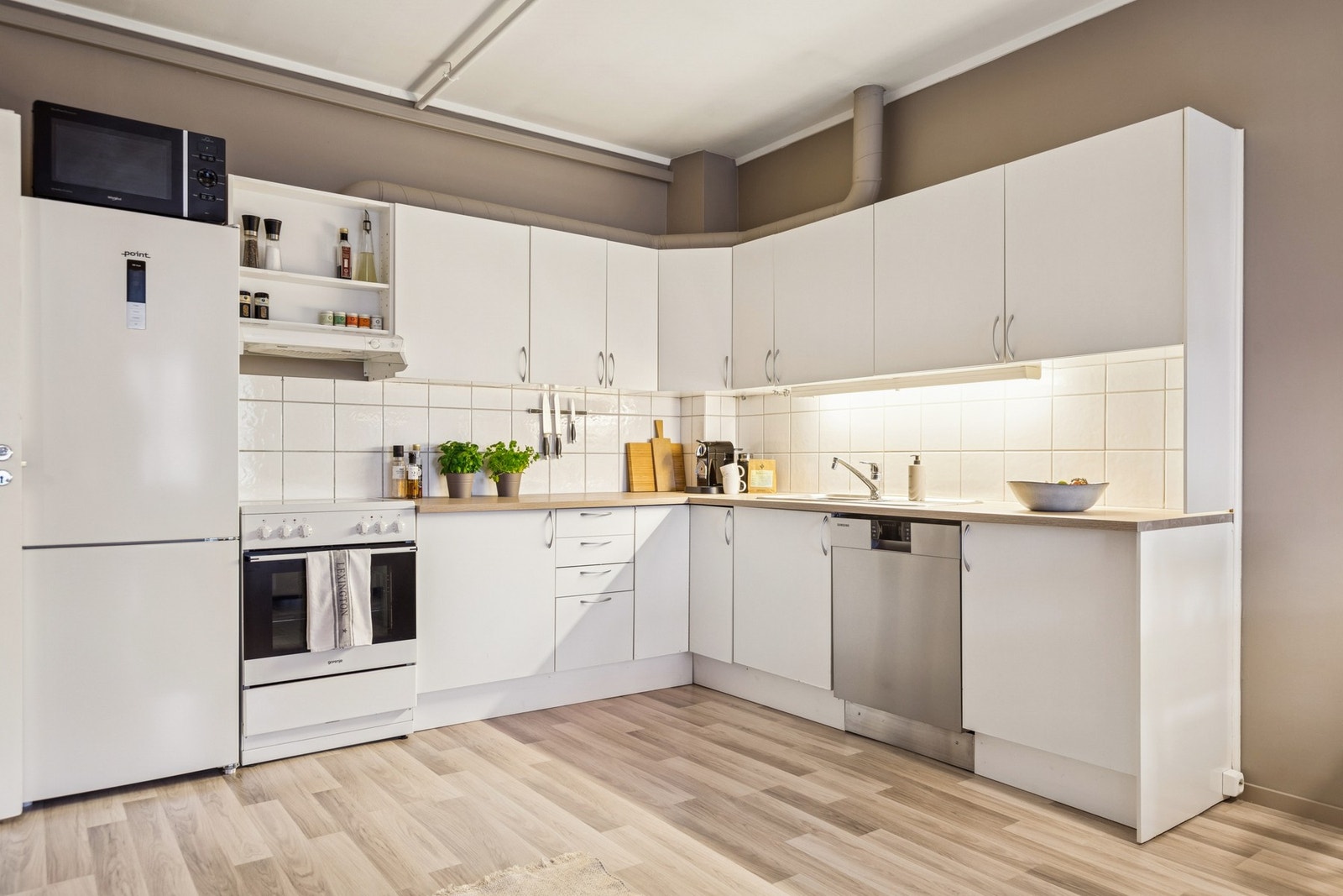 Kjøkkenet har hvite profilerte fronter, fliser mellom benk og overskap, og underbelysning. Galleribilde