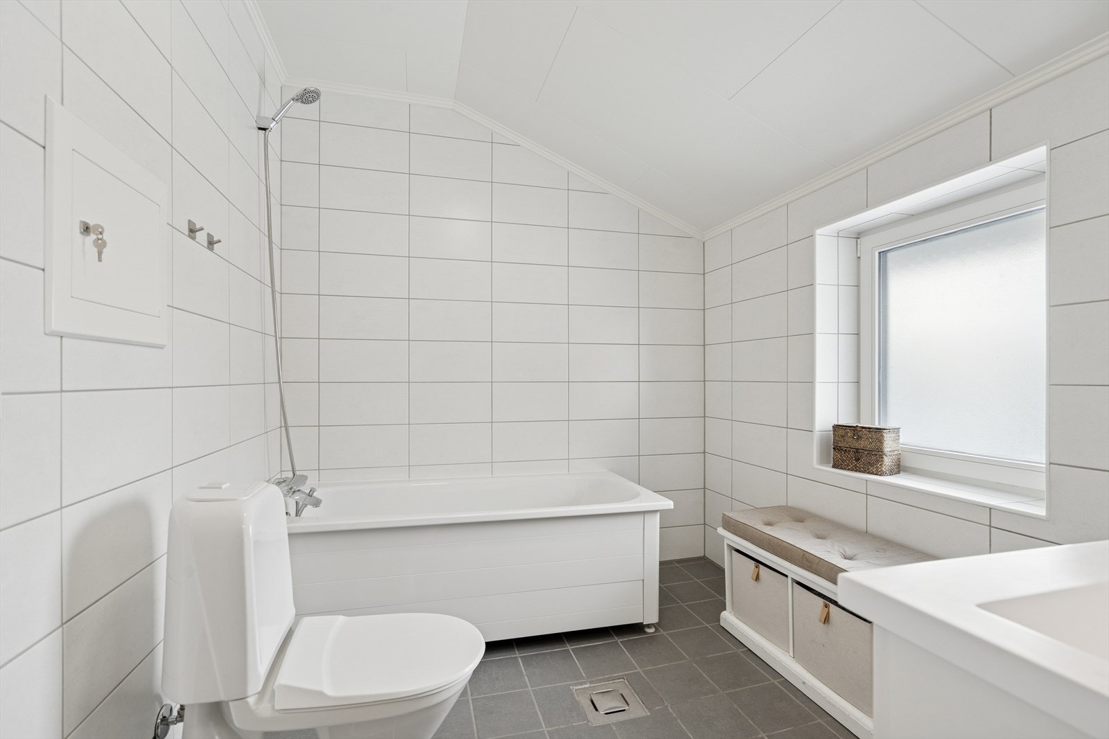 Badet har grå gulvfliser m/varmekabler under og hvite avlange veggfliser Galleribilde