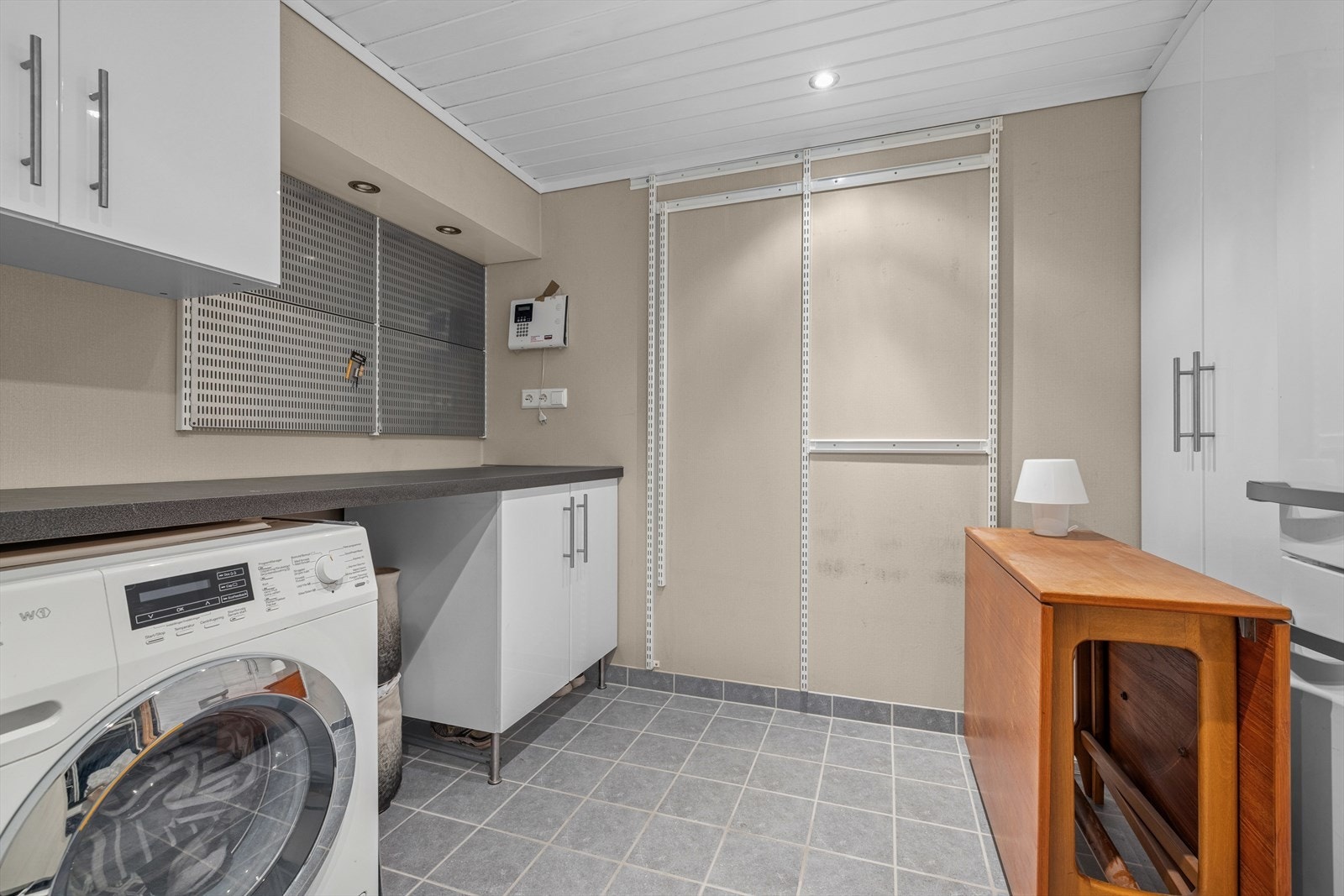 Vaskerommet har fliser på gulvet, malte veggplater og panel i taket. Rommet er innredet med benkeskap med vask og har opplegg for vaskemaskin. Galleribilde