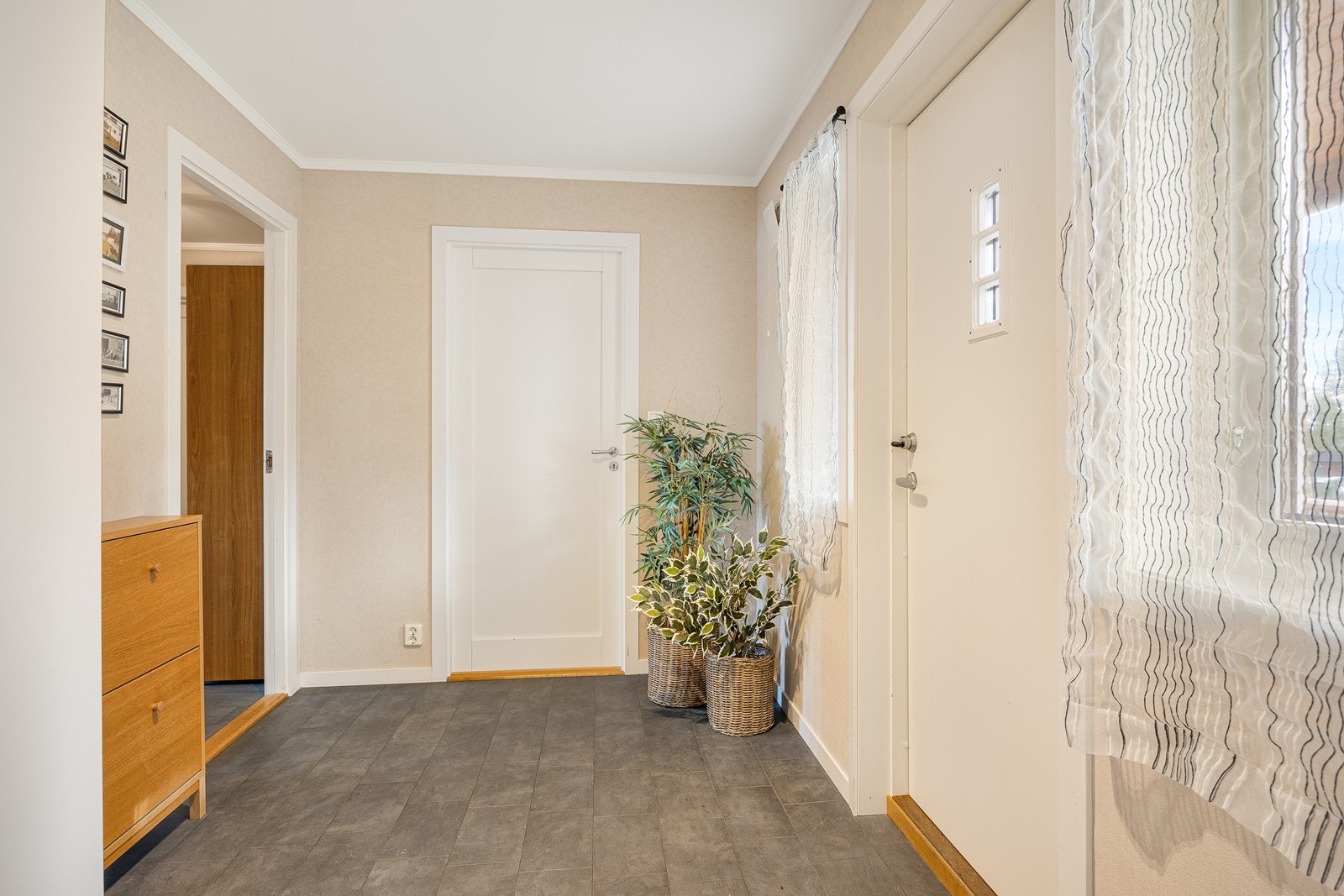 Vel inne er det en fin entré med lysmalte vegger og grått flislaminat på gulv med vannbåren gulvvarme - en komfortdetalj som er gjennomgående for hele første etasje. Galleribilde