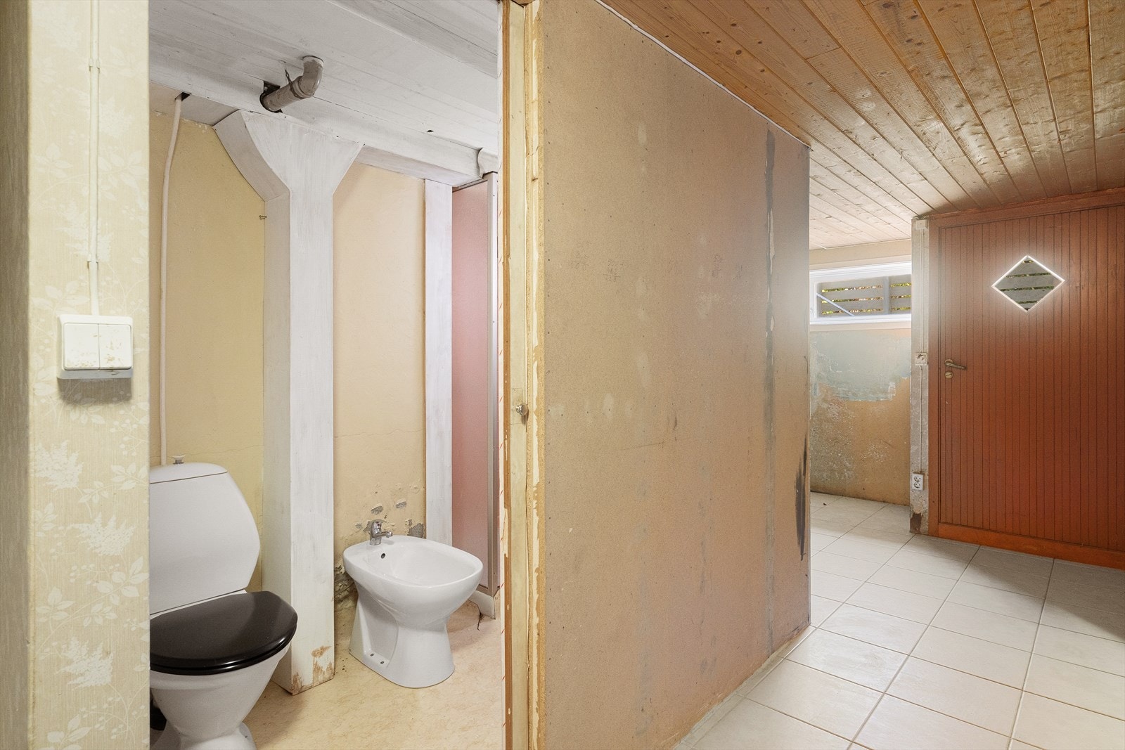 Romslig kjellerrom med toalett og bidé, klart for personlig tilpasning. Flislagt gulv og naturlig lysinnslipp. Galleribilde