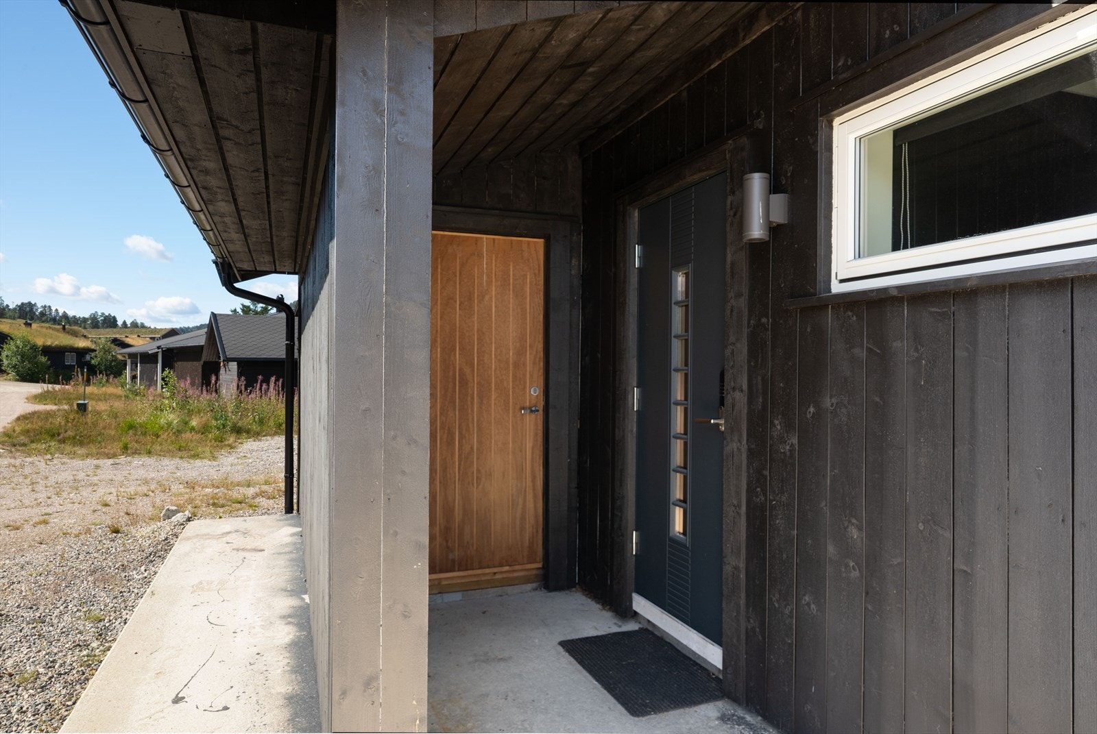 Støpt gangvei langs med hytteveggen fram til inngangspartiet som ligger med takoverbygg på sørøstsiden av hytta. Eier opplyser at det er lagt varmekabler i betongdekke ved inngangspartiet. Galleribilde