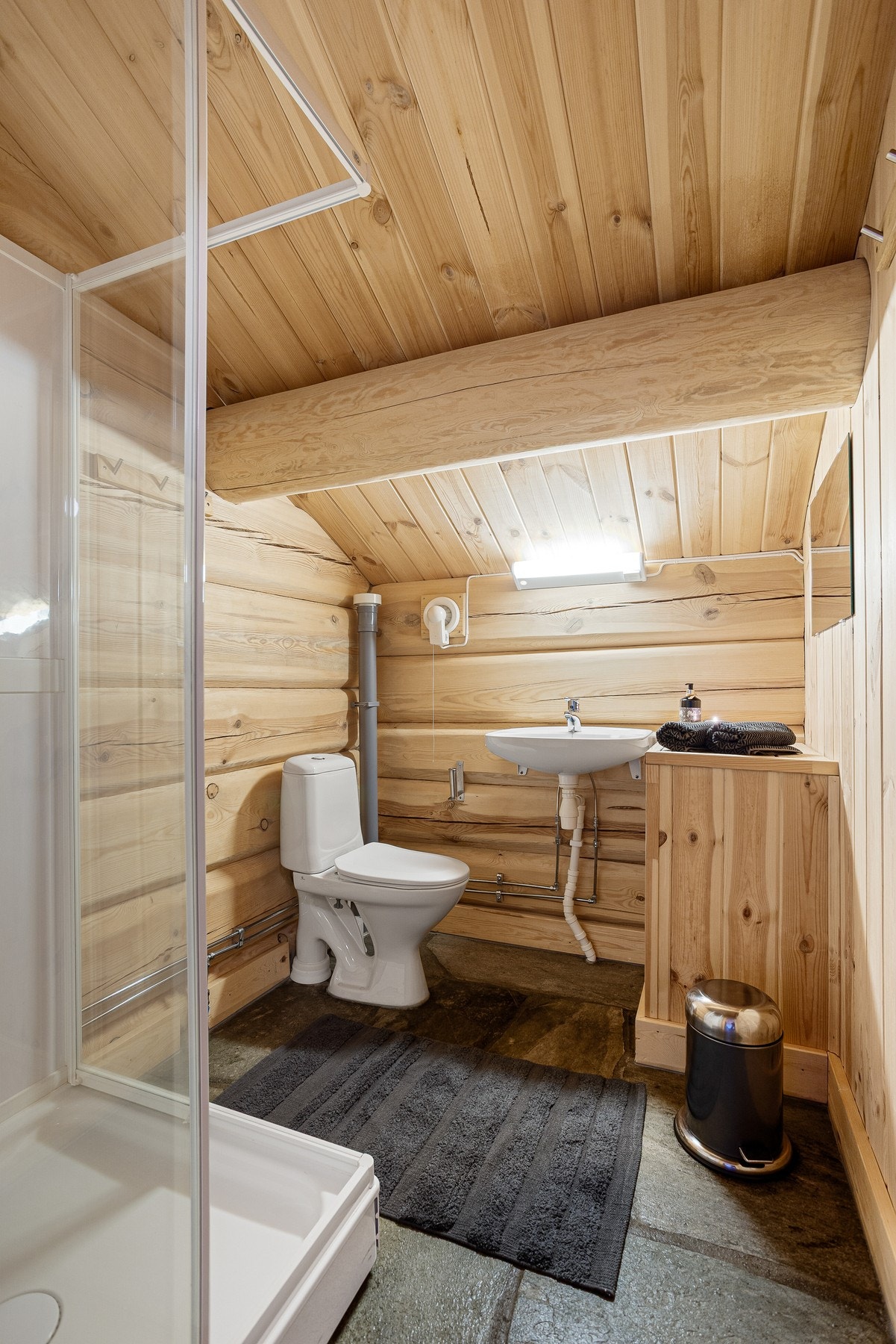Baderom i 2.etasje med toalett, servant og dusjkabinett. Skifer på gulv og tømmer på vegg Galleribilde