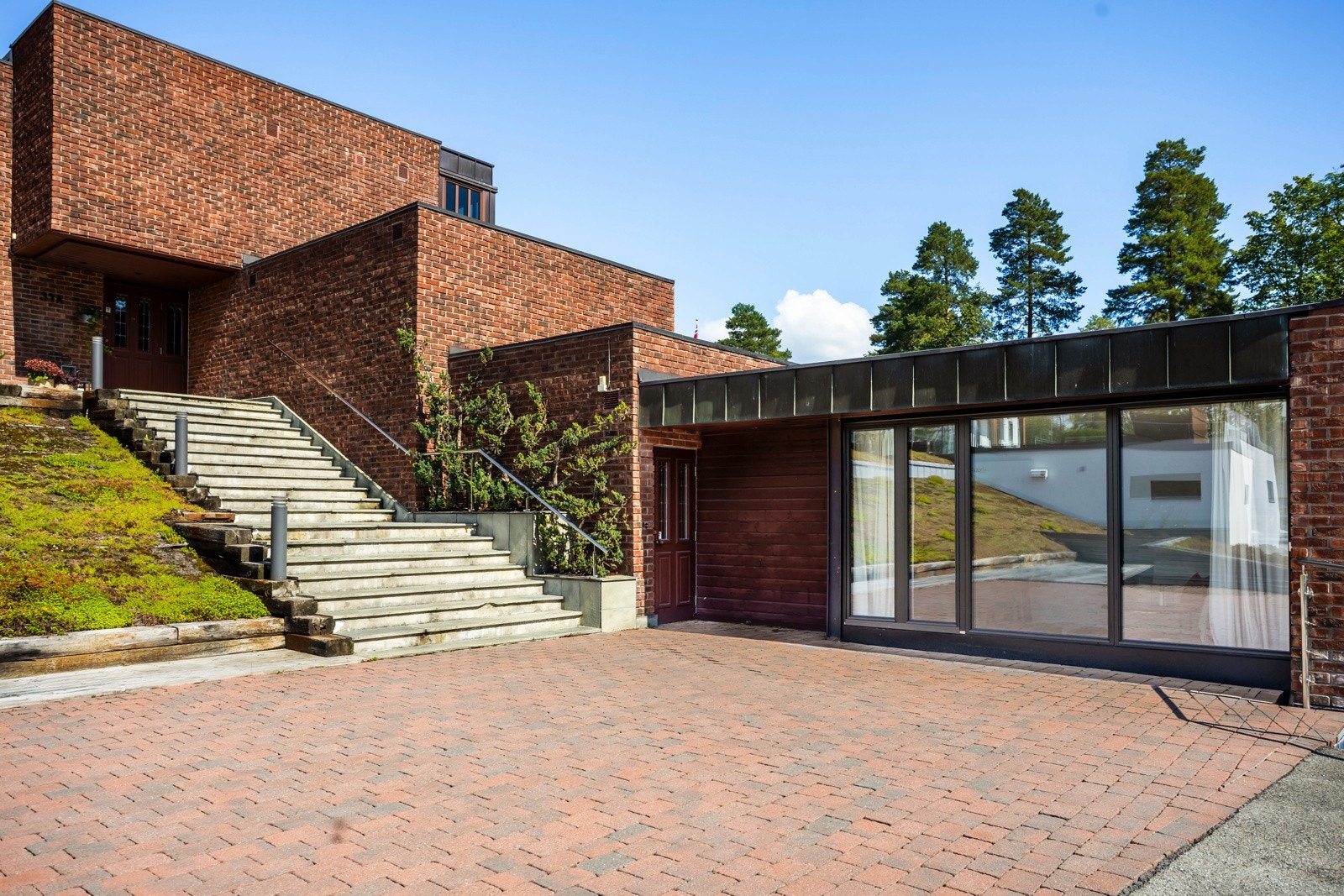 Bygningen er elegant tilpasset tomten, i måten den flukter terrenget og trinnvis kryper opp, for så å åpne seg opp på toppen av kollen m/store vindusflater mot utsikten og de gode lysforholdene. Galleribilde