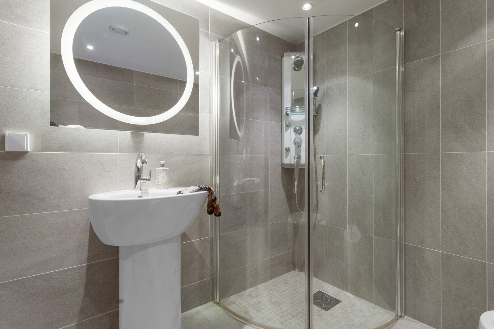 Badet i 1. etasje er innredet med dusjhjørne m/glassdører, servant (søilevask) og speil over servant samt toalett og bidé. Det er elektriske varmekabler i gulvet. Galleribilde