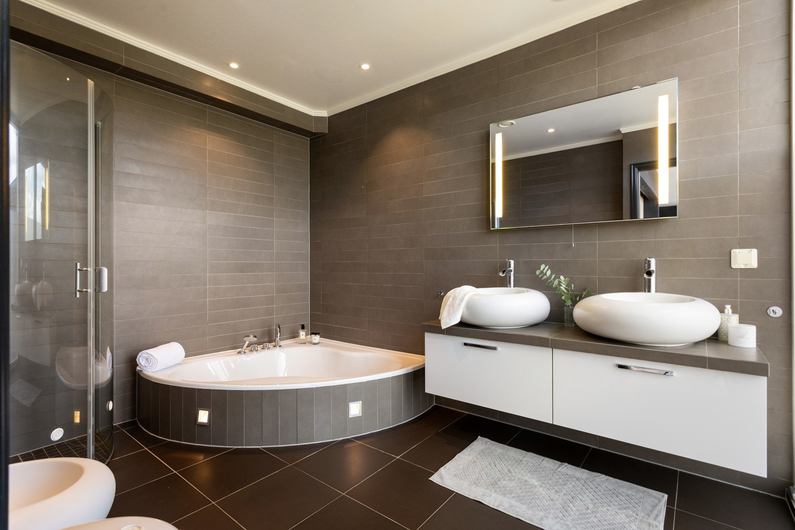 Badet ved hovedsoverommet har dusjhjørne med hengslede glassdører og innmurt badekar, vegghengt innredning med 2 stk. servanter (keramiske boller) og speil over servant samt vegghengt toalett og bidé. Elektriske varmekabler i gulvet. Galleribilde