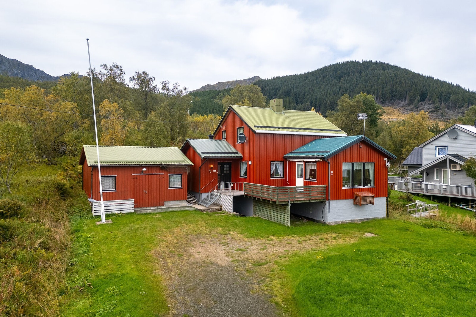 Fasade og uteområde. Rundt boligen er det opparbeidet tomt med plen, og delvis naturtomt med stedlig vegetasjon. Til venstre er uthuset fra ca. 1980. Galleribilde