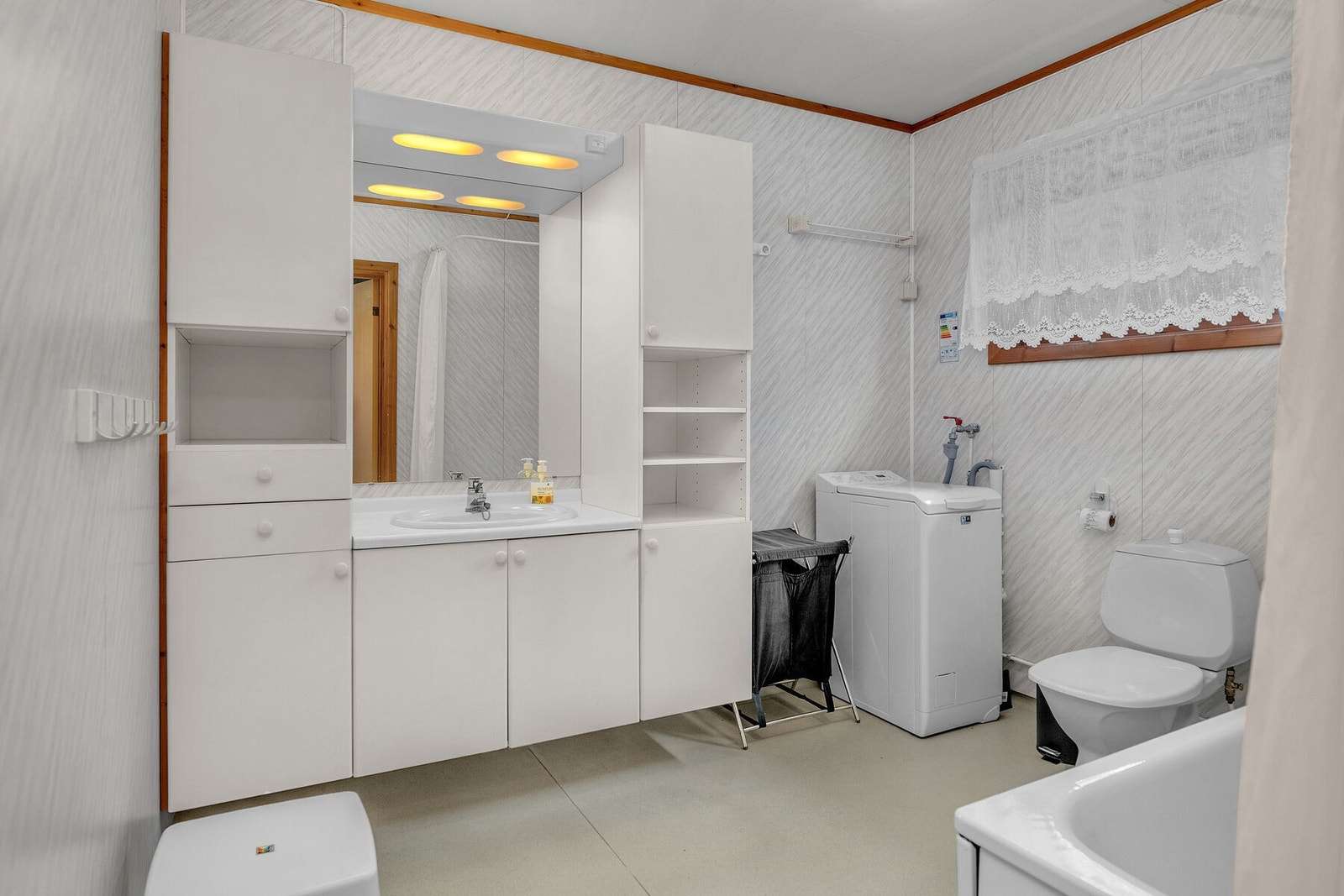 Bad/vaskerom fra 80-tallet, utført med baderomsplater på veggene, vinyl våtromsbelegg på gulv og himlingsplater i tak. Oppvarming ved elektrisk gulvvarme. Galleribilde