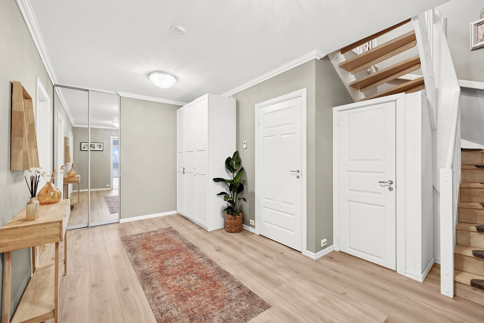 Via den pene trappen med eiketrinn kommer man ned i den store hallen i underetasjen. Her er det vannbåren gulvvarme. Praktiske garderobeløsninger og bod under trappen. Galleribilde