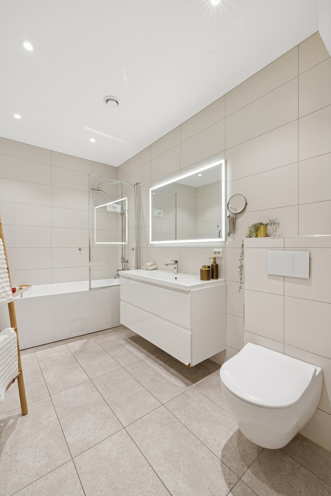 Det romslige badet har pene og store fliser både på gulv og vegger. Støpt gulv med vannbåren varme. Pen servantinnredning, speil med led lyslist og vegghengt toalett. Galleribilde