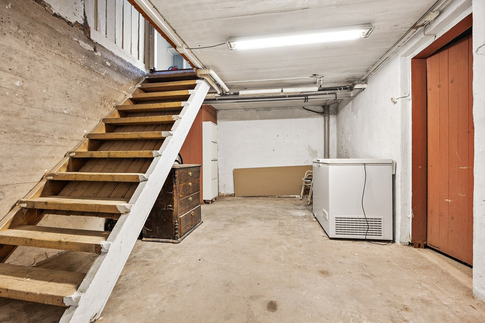 En enkel tretrapp leder ned til kjelleren, som inneholder flere boder, tekniske rom og et påbegynt bad. Galleribilde