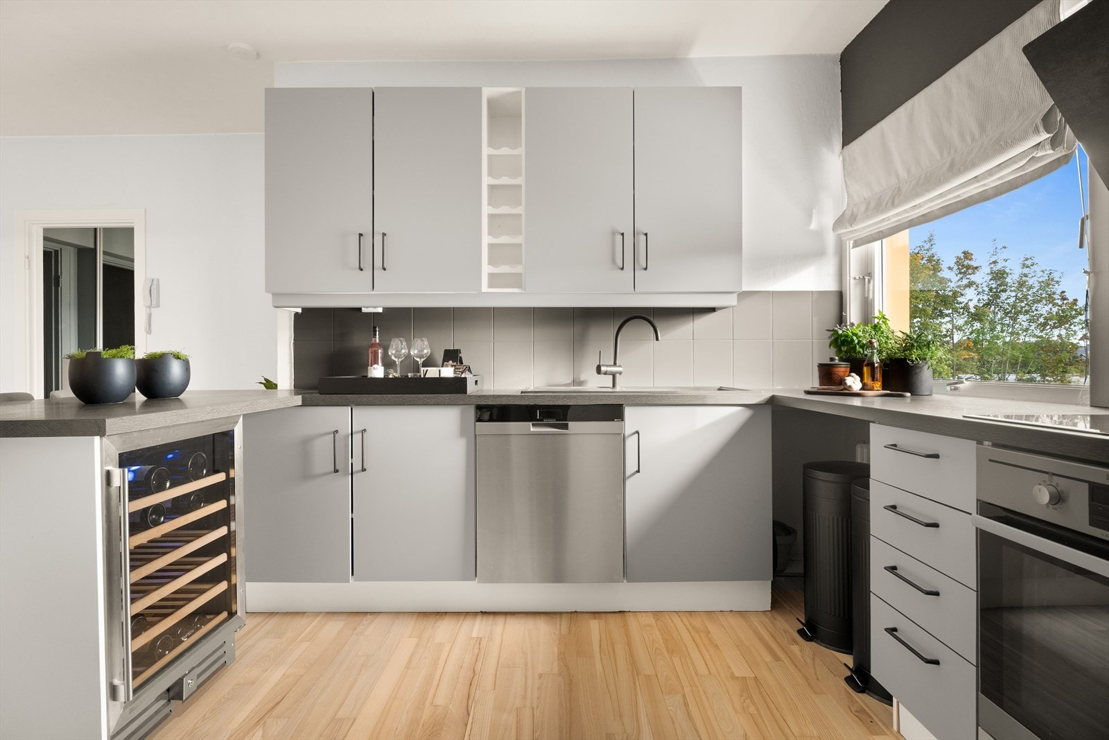 Kjøkken med grå slette fronter, laminert benkeplate og oppvaskkum. Fliser mellom benk og overskap. Galleribilde